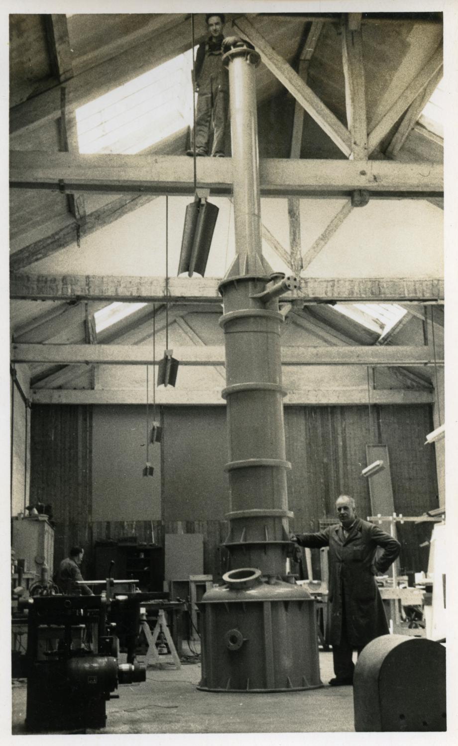Atelier de chaudronnerie plastique, au rez-de-chaussée. Tirage photographique noir et blanc, 8,5 x 13,5 cm, avant 1956 (date du décès de Jordi Planaguma i Gelada, ici perché sur la charpente), sans mention d'auteur (collection Ateliers de Technochimie).