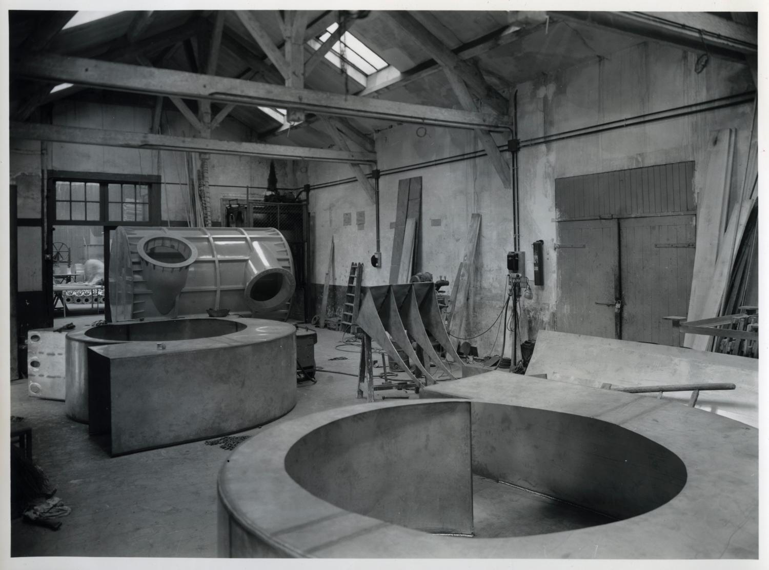 Atelier de chaudronnerie plastique, au rez-de-chaussée (aujourd'hui atelier de réception des matières premières). À l'arrière, tour de lavage en PVC, à l'avant, corps de ventilateur métallique. Tirage photographique noir et blanc, 18 x 24 cm, années 1960, sans mention d'auteur (collection Ateliers de Technochimie).