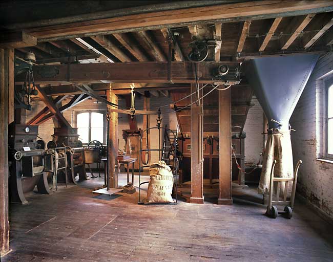 Atelier principal, 1er étage, salle des broyeurs, vue intérieure. De gauche à droite : broyeurs, balance à fléau, chambre à farine, ensacheuse.