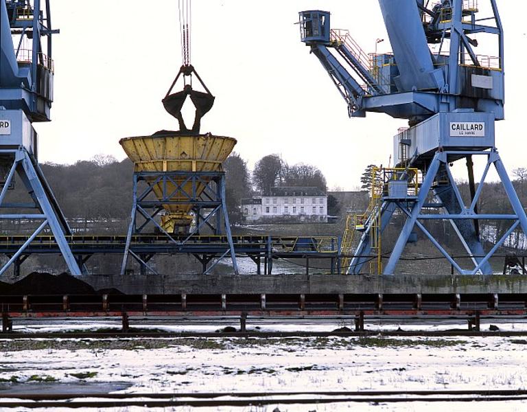 Grue déchargeant le charbon dans une trémie installée sur un convoyeur à bandes.