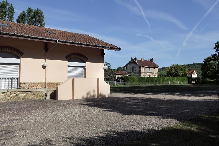 Vue partielle de la halle à marchandises avec la gare et ses latrines à l'arrière plan.