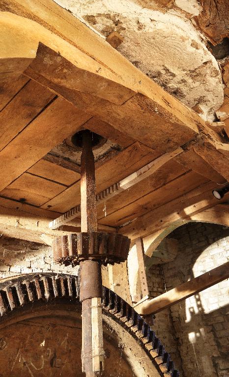 Vue intérieure du moulin : beffroi, engrenage, axe de transmission et meule dormante.