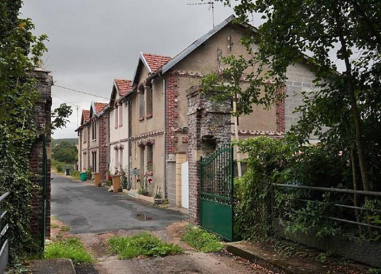 Vue générale des maisons ouvrières jumelées depuis la passerelle sur l'Andelle donnant accès au site.