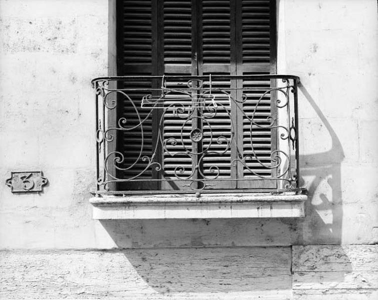 Premier étage, grille de balcon en fer forgé avec motif central en fonte.