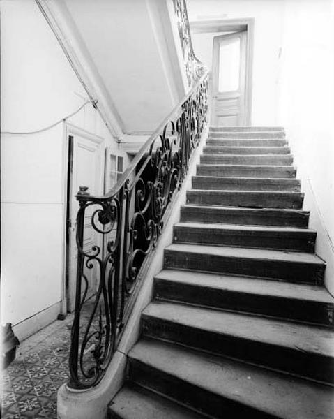 Escalier dans oeuvre, en bois avec rampe de fer forgé, niveau rez-de-chaussée.