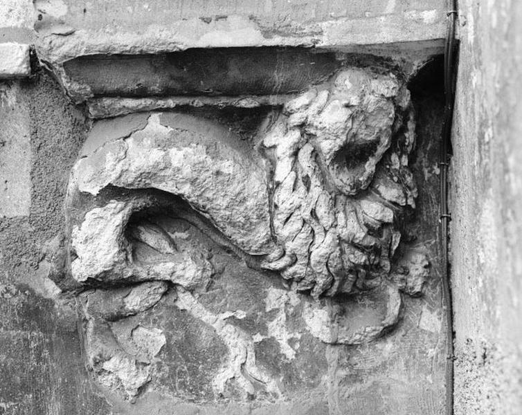 Bâtiment ouest, façade est. Baie du rez-de-chaussée, détail : élément sculpté (lion) sous un pilastre.