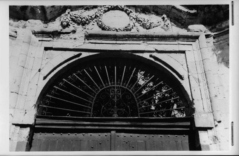 Portail d'entrée monumental détail : la grille du tympan armoriée et décor sculpté de guirlandes de fruits et de laurier.