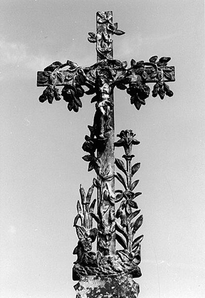 Cimetière : vue de détail d'une croix avec un Christ, ornée de roses, lys et joncs (1924).