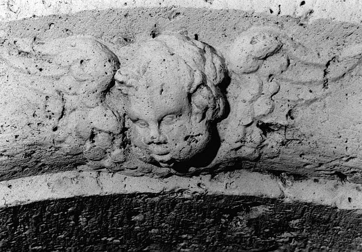 Vue de détail de l'angelot sculpté sur l'arc de la porte du clocher, du nord.