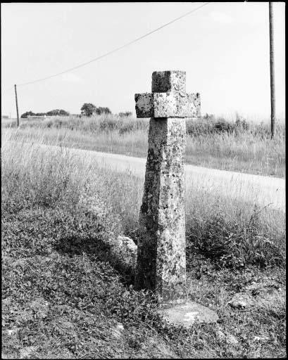 Croix de chemin en pierre avec inscription et fleur sculptée.