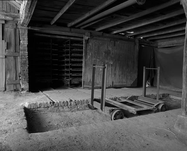 Entrée de la halle de séchage à laquelle on accède par la grande porte coulissante en bois, chariot en bout de chaîne apportant les briques façonnées.