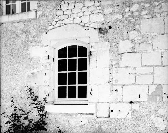 Logis, détail dela baie à gauche de la porte d'entrée, surmontée del'inscription rebâti en 1790. On distingue encore l'emplacement de la baie primitive, chanfreins à gauche et départ du meneau à droite, prouvant que l'ouverture a été rétrécie au XVIIIe siècle.