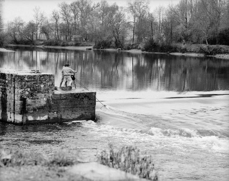 Pour relever le barrage, on dresse successivement les fermettes couchées au fond de l'eau au moyen de chaînes et d'un petit treuil mobile. Ici, le relevage de la première fermette, appelée fermette de rive.