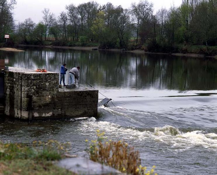 Pour relever le barrage, on dresse successivement les fermettes couchées au fond de l'eau au moyen de chaînes et d'un petit treuil mobile. Ici, le relevage de la première fermette, appelée fermette de rive.