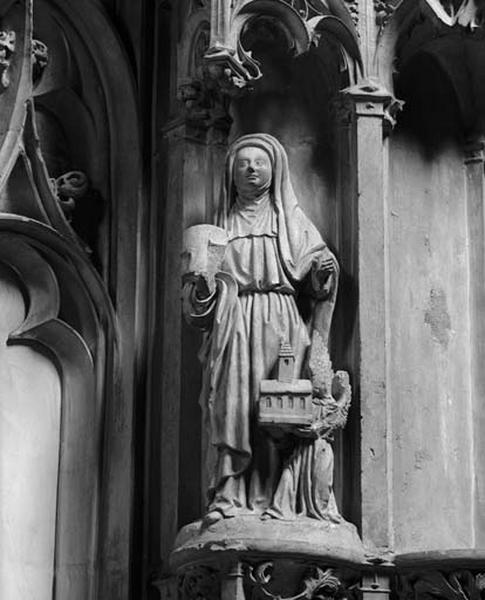 Contrefort de jonction entre la première et la deuxième travées sud, étage inférieur : religieuse tenant un livre de prières. A ses côtés, un ange de petite taille présente une maquette de chapelle.