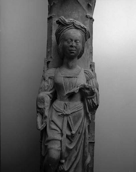 Troisième travée sud, pilastre de jonction entre la deuxième et la troisième sections, étage médian : statuette de revers, femme élégamment vêtue et coiffée d'un turban tenant un livre ouvert dans la main gauche (vue de face). Le bras droit a disparu.