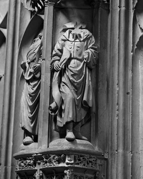 Quinzième travée nord, petit contrefort de jonction entre la première et la deuxième sections, étage inférieur, statuette droite : homme portant une barbe à plusieurs pointes, vêtu d'une tunique boutonnée et chaussé de bottes. Il tient un phylactère déroulé. La tête et la main gauche ont disparu. Une statuette portant une barbe analogue se trouve dans la treizième travée nord à l'étage médian.