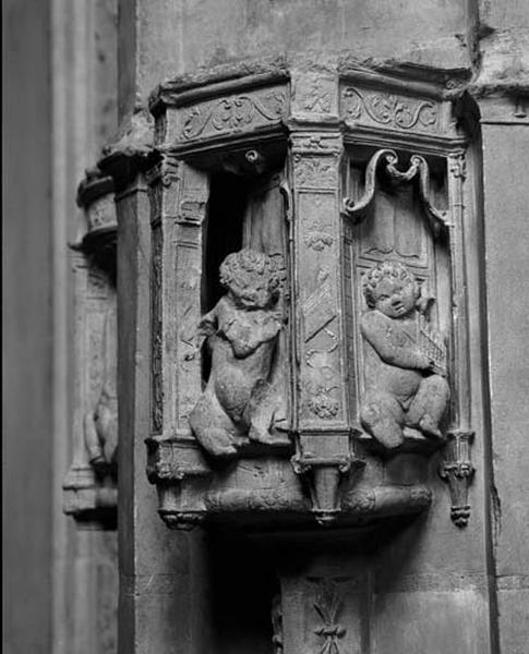 Contrefort de jonction entre la dixième et la onzième travées nord, chapiteau de colonnette cul-de lampe du milieu : dans une architecture de théatre, des putti musiciens jouent, l'un d'un orgue portatif, l'autre devait jouer de la flûte (disparue).