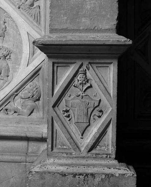 Cinquième travée sud, pilastre de jonction entre les deux sections, face du socle : Sainte Chemise de la Vierge timbrée sur un cuir découpé inscrit dans un losange.