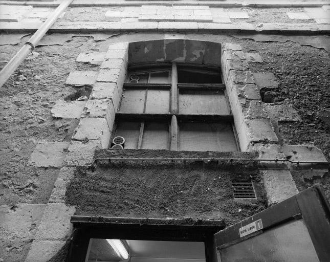 Baie partiellement bouchée avec reste du croisillon de bois d'origine au rez-de-chaussée de la façade ouest du corps de bâtiment perpendiculaire à la collégiale.