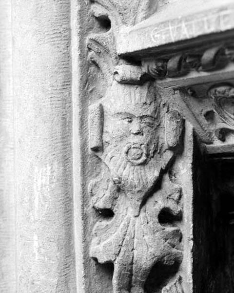 Troisième travée sud, première section, au-dessus de la petite fenêtre grillée : mascaron posé sur une feuille et tenant l'anneau de la chute dans la bouche.