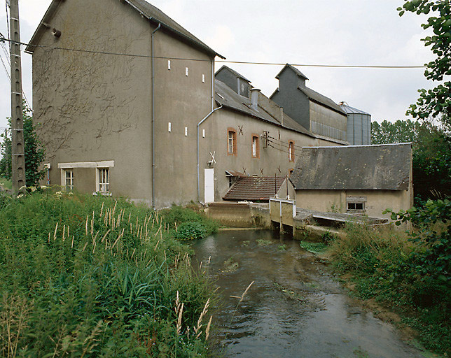 Vue du moulin prise de la rive gauche de la dérivation (du nord-ouest). Au premier plan, à droite, le déversoir. A gauche, bâtiment comptant deux étages ajouté à la fin des années 1940.