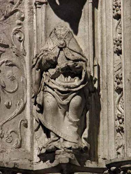 Troisième travée sud, claire-voie de la troisième section, arc en anse de panier soulignant l'ancienne ouverture sur le choeur, côté gauche : ecclésiastique assis en haut-relief situé au départ de l'arc, revêtu d'une chape richement ornée, il tient un livre ouvert de la main gauche et devait écrire de l'autre main (la tête et les mains ont disparu).