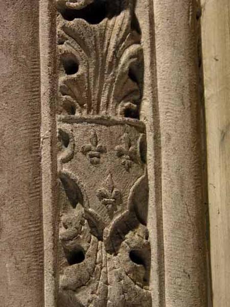 Troisième travée sud, claire-voie de la première section, encadrement gauche de la première baie : cuir découpé posé sur des feuilles d'acanthe et portant trois fleurs de lys.