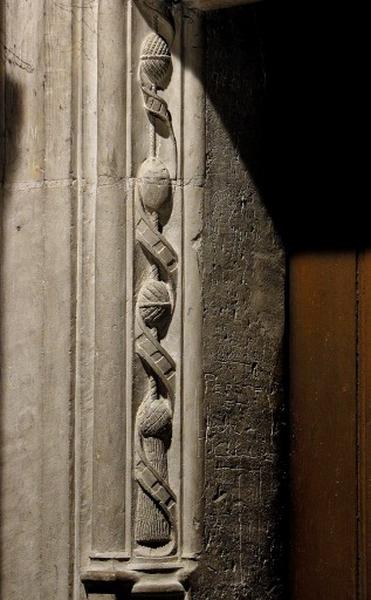 Troisième travée sud, encadrement de la porte de la quatrième section, côté gauche : chute composée d'un ruban orné de petits carrés en relief et enroulé autour de glands reliés par une cordelette.