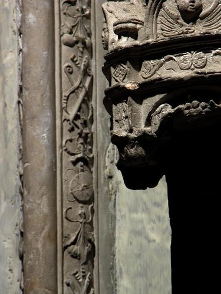 Quatrième travée sud, claire-voie de la première section, premier meneau : détail de la chute d'objets, deux chenets entrecroisés et un couvercle (?) séparés par des bouquets de fleurs et entrelacés de rubans. A droite, le dais surmontant une niche de statuette.