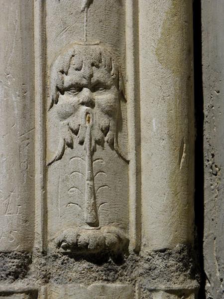 Sixième travée sud, claire-voie de la première section, encadrement gauche de la première baie : mascaron soufflant dans une flûte.