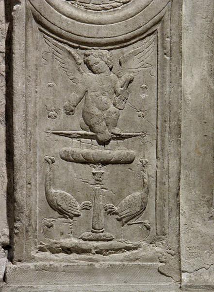 Cinquième travée sud, soubassement de la deuxième section, petit pilastre central : un putto assis sur un vase à pied et entouré par deux oiseaux opposés, joue de la viole, des guirlandes de fleurs gravées pendent de ses ailes.