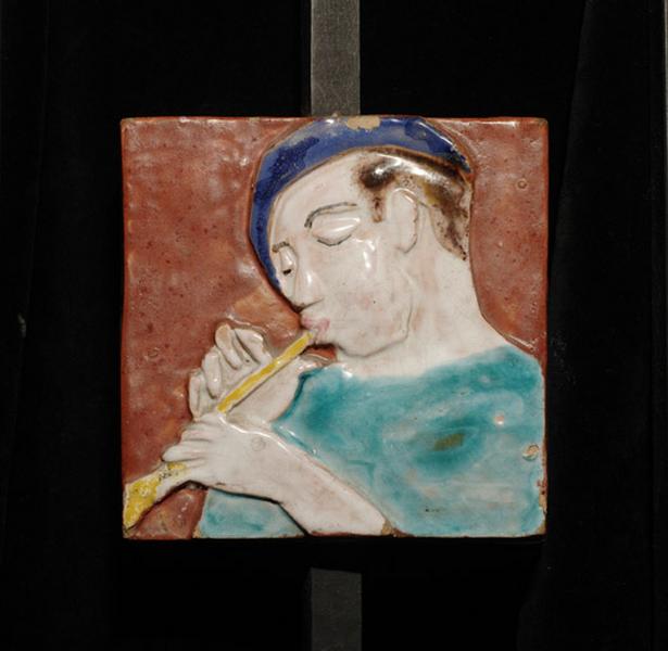 Plaque ornée d'un joueur de pipeau coiffé d'un béret.