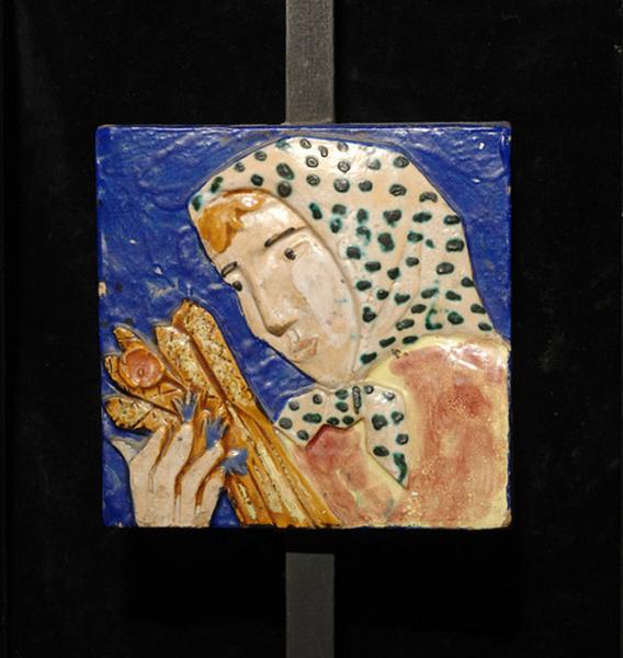 Plaque ornée d'une paysanne, la tête couverte d'un fichu, portant une gerbe de blé.