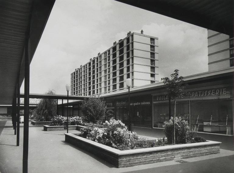Vue du centre commercial et du bâtiment K en direction du sud-ouest - 1962. (Archives départementales d'Indre-et-Loire, section contemporaine, Chambray-lès-Tours, Série Fi, cote 5Fi-P35, 17956-2). ; Vue de l'ancien centre commercial et du bâtiment K - 1962. (Archives départementales d'Indre-et-Loire, section contemporaine, Chambray-lès-Tours, Série Fi, cote 5Fi-P35, 17956-2).