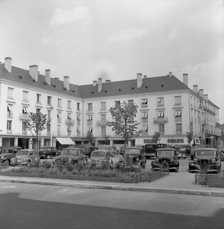 Vue des façades donnant sur la place de la Résistance et la rue du Maréchal-Foch, mai 1954. (ministère de l'écologie, du développement durable, des transports et du logement, Fonds M.R.U., cliché n°20377). ; Vue des façades de l'îlot E sur la place et la rue du Maréchal-Foch, mai 1954. (ministère de l'écologie, du développement durable, des transports et du logement, Fonds M.R.U., cliché n°20377).