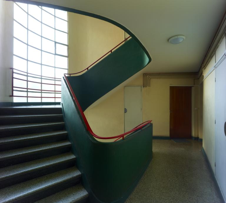 Escalier en béton éclairé par une baie toute hauteur.