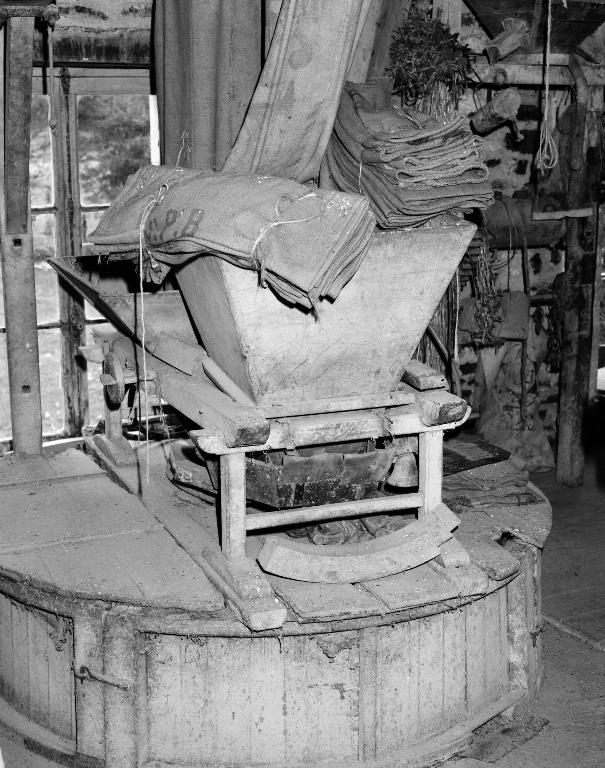 Intérieur de l'atelier de fabrication, trémie et meules dans leur archure, plan rapproché.