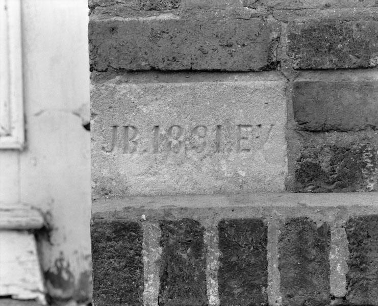 Logement (2). Elévation extérieure nord-est. Détail : initiales des commanditaires (Jacques Brière et E. V.), et date de construction (1891).
