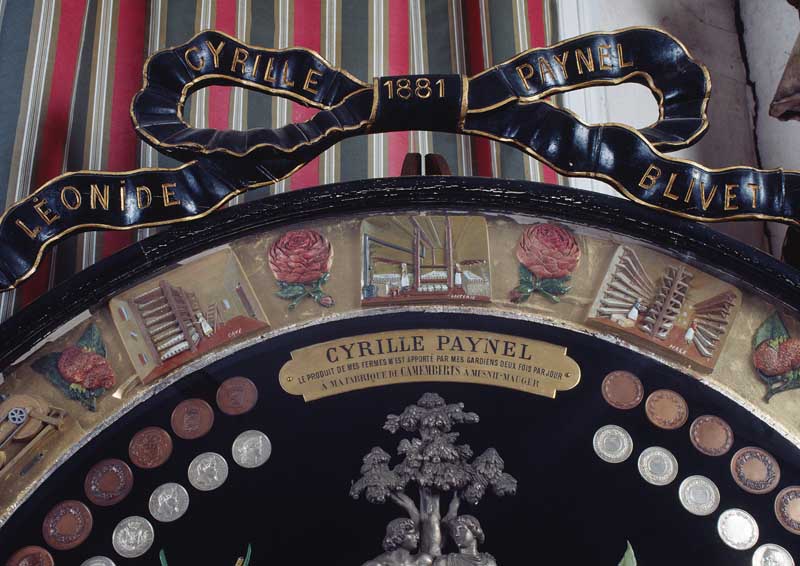 Détail de la partie haute : inscription et date se rapportant aux destinataires du trophée, et représentation des caves, laiterie et hâle.