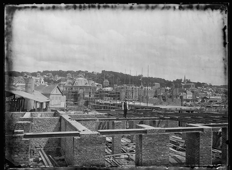 'Chantier de construction. Casino de Trouville. Vue prise du côté restaurant. Trouville en arrière-plan.- Photographie ancienne, n.s., 30 juillet 1911. Tirage n.et b. d''après plaque de verre gélatino-bromure d''argent (négatif), 13 x 18 cm. (Musée municipal, Villa Montebello, Trouville-sur-Mer. 006.1.5 ; 006.1.6).'