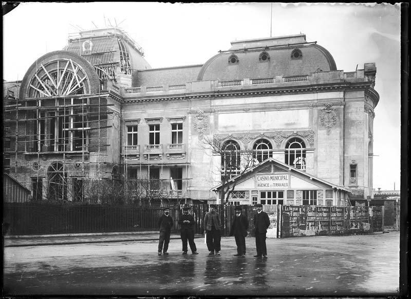 'Chantier de construction. Casino de Trouville. Vue prise de la place, avec l''agence des travaux et un groupe de personnes. Vue de la façade nord-est.- Photographie ancienne, n.s., n.d., 1911. Tirage n. et b. d''après plaque de verre gélatino-bromure d''argent (négatif), 13 x 18 cm. (Musée municipal, Villa Montebello, Trouville-sur-Mer. 006.1.43).'