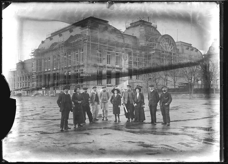 'Chantier de construction. Casino de Trouville. Vue prise du marché, avec un groupe de personnes. Vue des façades sud-est et nord-est.- Photographie ancienne, n.s., n.d., 1911. Tirage n. et b. d''après plaque de verre gélatino-bromure d''argent (négatif), 13 x 18 cm. (Musée municipal, Villa Montebello, Trouville-sur-Mer. 006.1.44).'