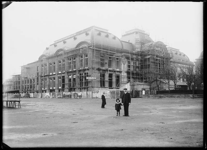 'Chantier de construction. Casino de Trouville. Vue prise du marché, avec un homme et fillette posant. Vue des façades sud-est et nord-est.- Photographie ancienne, n.s., n.d., 1912. Tirage n. et b. d''après plaque de verre gélatino-bromure d''argent (négatif), 13 x 18 cm. (Musée municipal, Villa Montebello, Trouville-sur-Mer. 006.1.48).'