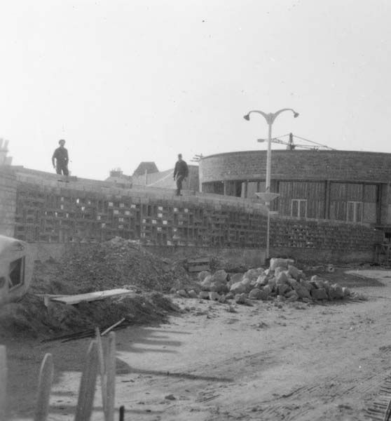 'Reconstruction du casino. Mur reliant le casino au pavillon d''information. Vue d''ensemble prise du nord-est.- Photographie ancienne, n.s., 15 mars 1957, [date manuscrite]. Tirage original sur papier brillant contrecollé sur carton, n. et b., 6,2 x 6,2 cm. (AC Ouistreham).'