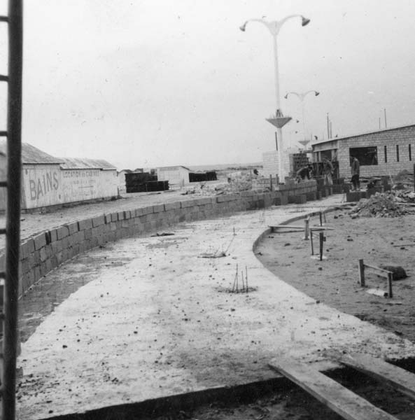 'Reconstruction du casino. Mur reliant le casino au pavillon de l''information, vue prise de l''ouest.- Photographie ancienne, n.s., 1er février 1957, [date manuscrite]. Tirage original sur papier brillant contrecollé sur carton, n. et b., 6,2 x 6,2 cm. (AC Ouistreham).'