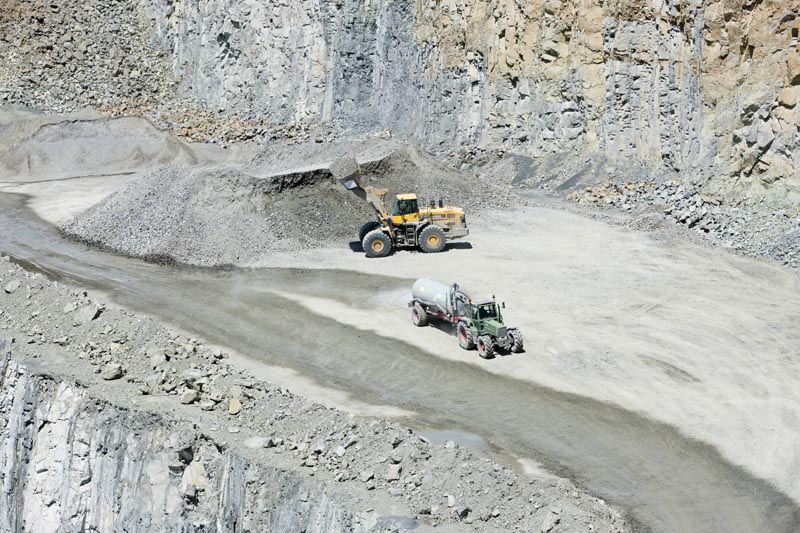Pelle attendant de charger un dumper et camion citerne assurant l'humidification des pistes.