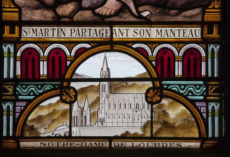 Détail de la baie 1 : légende de la scène et représentation de la basilique Notre-Dame-de-Lourdes.