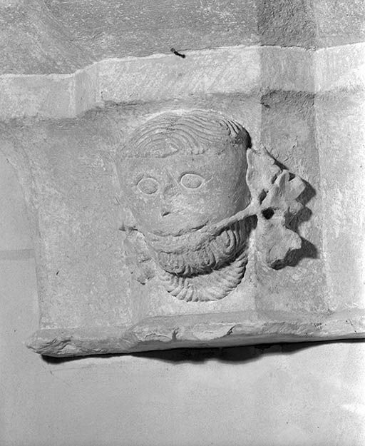Bas-côté gauche, entre la 1ère et la 2e travée. Culot sculpté d'une tête d'homme grimaçante tenant une branche dans sa bouche.