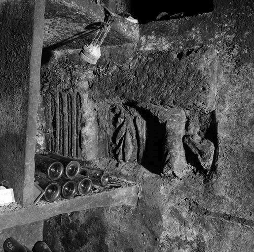 Bâtiment sud : cave, caveron du 1er vaisseau, fragments de reliefs gallo-romains remployés dans un casier à bouteilles, vue prise en lumière rasante